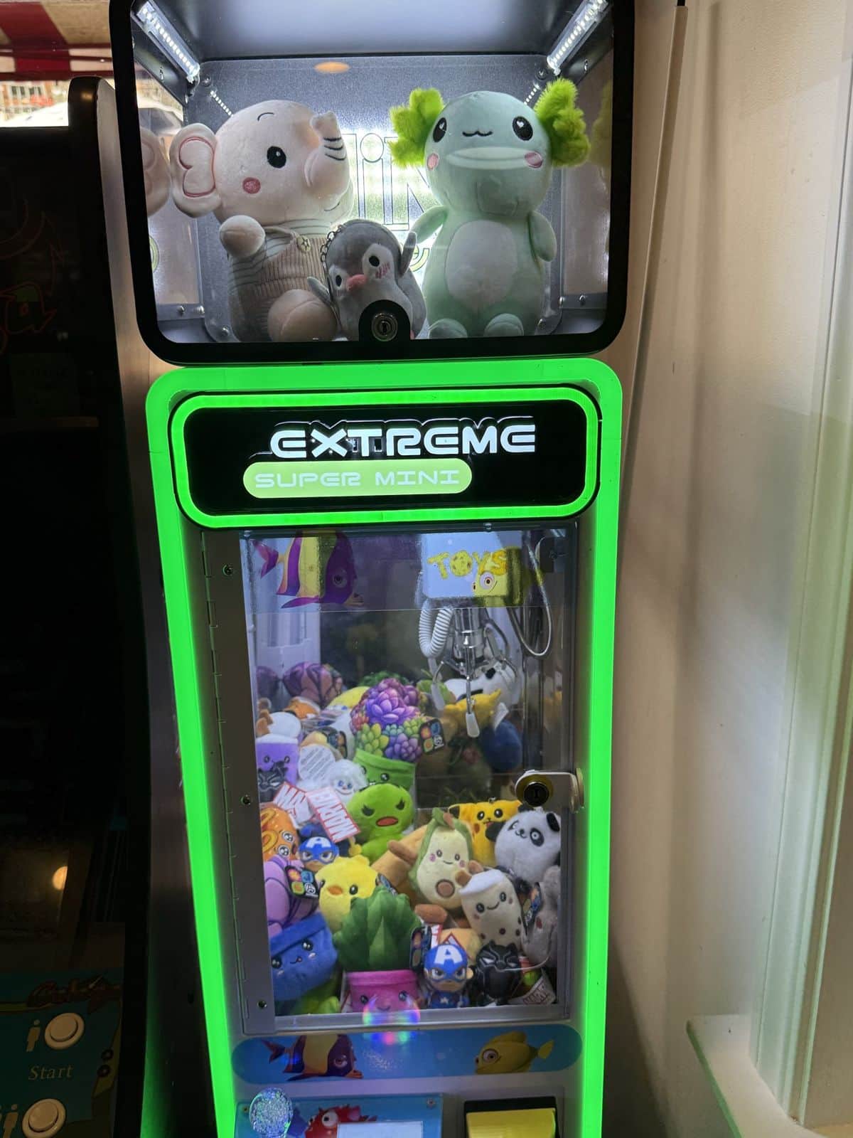A green-lit claw machine in a diner, an elephant and an axolotl plush in the display box on top