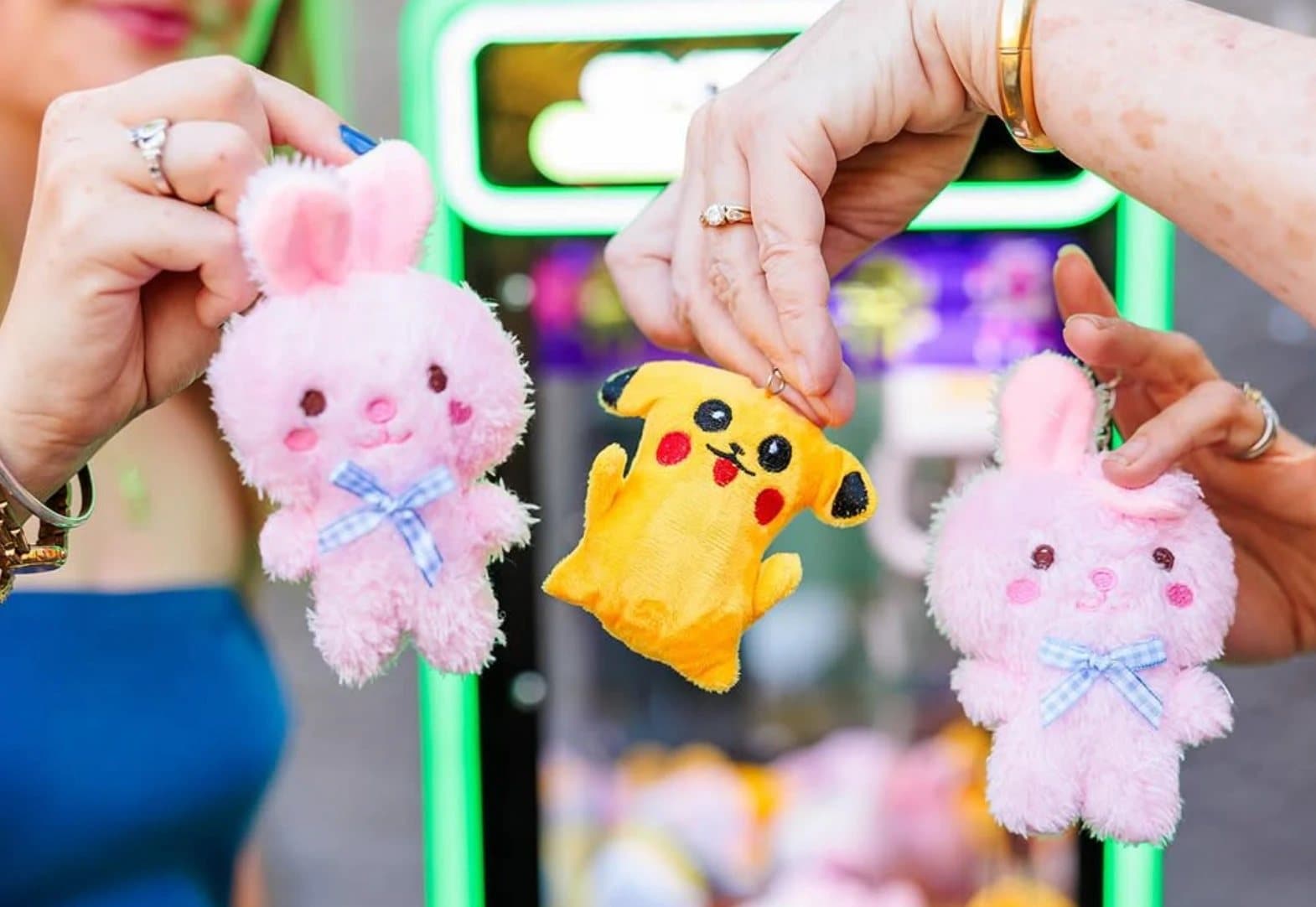 Three people holding plushies they won — two pink bunnies and a Pikachu — in front of a California Claw machine