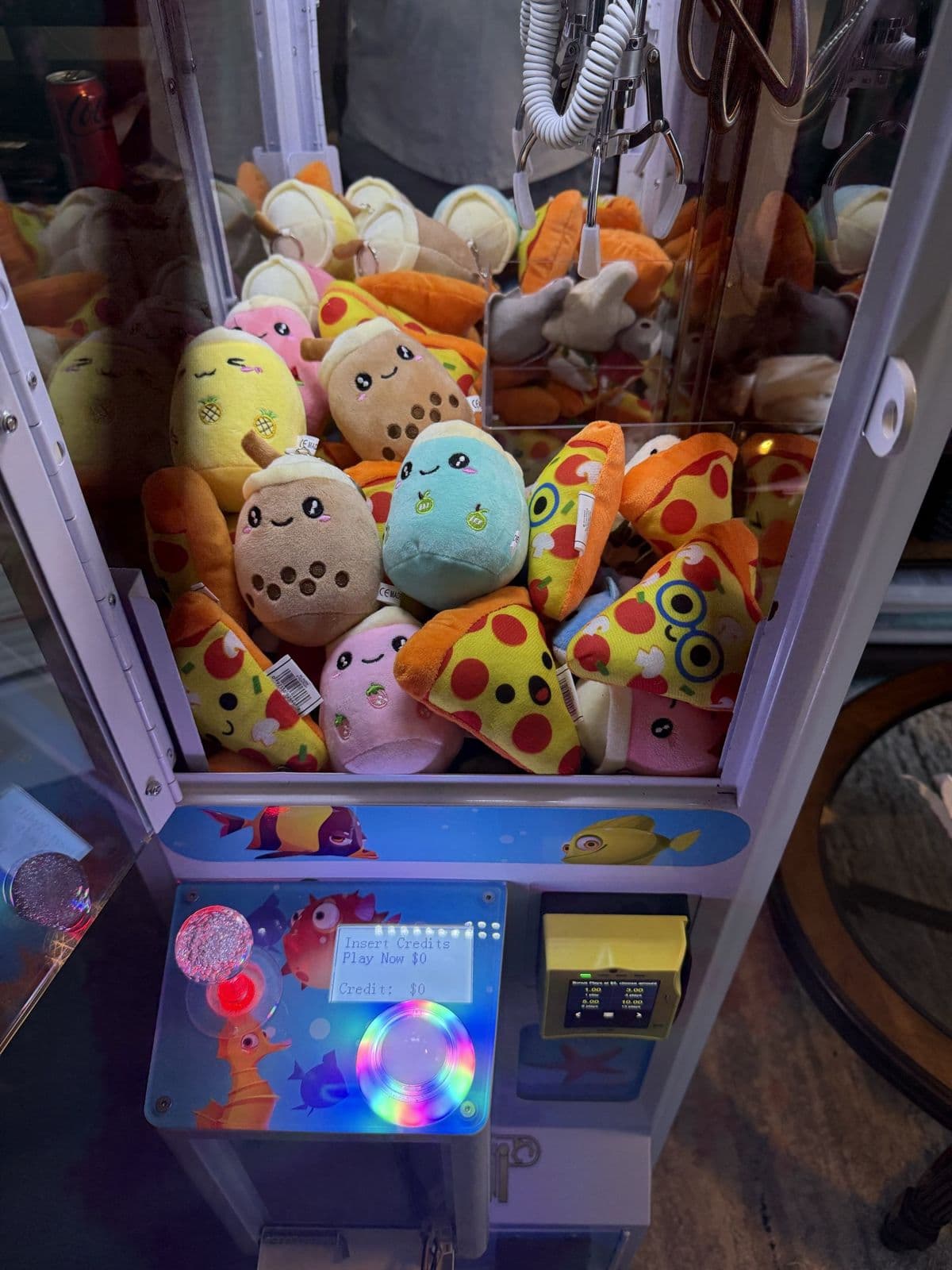 Close-up of a claw machine stocked with pizza-slice and boba-cup plushies