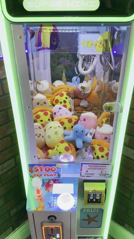 A neon-green California Claw machine in a pizzeria, packed with plush prizes
