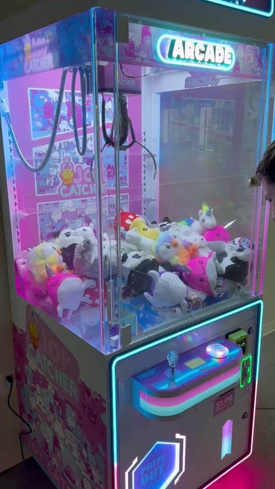 A neon Joy Catcher claw machine in a tea house, the claw moving over a pile of plush